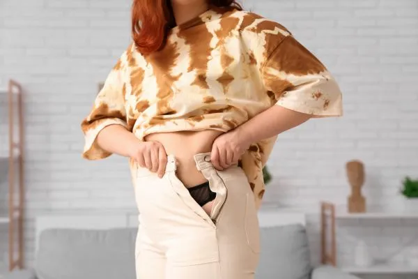 Image of woman trying to do her trousers up after pregnancy weight gain Bagshot